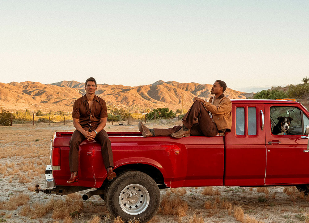 Two men sitting in a red truck with a dog wearing Tony Lama boots: Galán 13" brown cowboy boots and 13" brown Nile crocodile Kango boots.